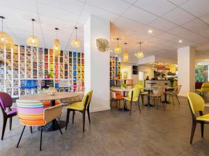 un restaurant avec des chaises et des tables colorées et une cafétéria dans l'établissement ibis Styles Perpignan Centre Gare, à Perpignan