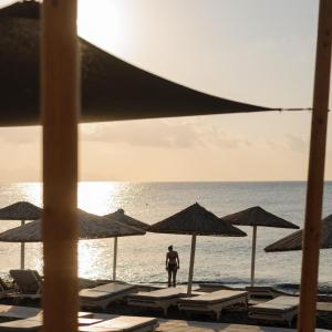 Ein Mann steht am Strand mit Stühlen und Sonnenschirmen in der Unterkunft Afroditi Venus Beach Resort in Kamari