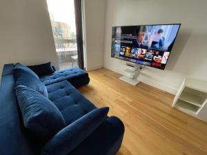 Luxury Top Floor Penthouse Apartment near Heathrow في لندن: غرفة معيشة مع أريكة زرقاء وتلفزيون بشاشة مسطحة