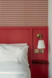 a red wall with a white bed and a lamp at St. David's Hotels Paddington in London