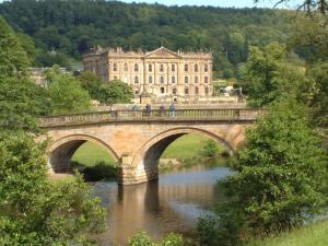 a bridge over a river in front of a large building at Nook Cottage, Hot Tub, Polar Bears, Alton Towers, Bakewell, Chatsworth House, Peak District Stay in Foxt