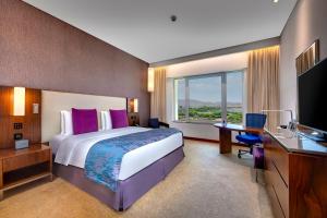 um quarto de hotel com uma cama grande e uma televisão em Crowne Plaza Muscat OCEC, an IHG Hotel em Mascate