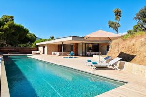 a swimming pool with chairs and an umbrella next to a house at Hotel Bartaccia in Propriano