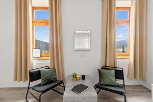a living room with two chairs and a table and two windows at StayEasy Apartments Sankt Michael #1 in Sankt Michael in Obersteiermark