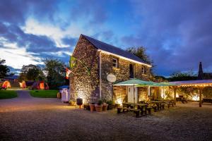 a stone building with picnic tables and umbrellas at night at Podumna Glamping Village in Portumna