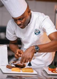 un chef que prepara comida en un plato en una cocina en Cap Kivu Hôtel, en Goma