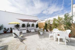 eine Terrasse mit weißen Stühlen, Tischen und einem Sonnenschirm in der Unterkunft Villetta Iris by Vivimy in Taviano