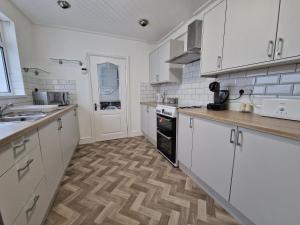 a kitchen with white cabinets and a wooden floor at Oasis 3 Bedroom Home Near Town Centre with garage for bike storage in Dowlais