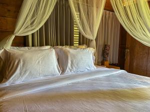 a bed with white pillows and curtains in a bedroom at Bidja Room Wooden Joglo House in Sempidi