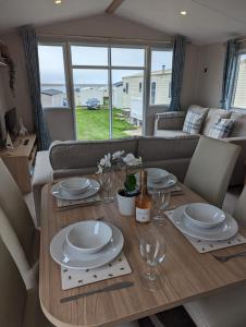 a dining room table with plates and wine glasses at Stylish Modern Bright Caravan with Views sleeps 6 Littlesea Haven Weymouth in Weymouth