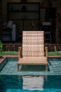 Una silla de mimbre sentada junto a una piscina. en Nossa Villa Caraíva, en Caraíva