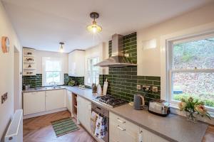 uma cozinha com armários brancos e azulejos verdes na parede em Gardeners Cottage em Challoch