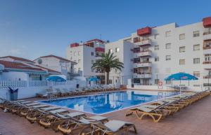 una piscina con sillas y sombrillas junto a los edificios en Apartamentos Tinerfe Garden, en Adeje