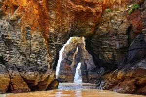 eine Höhle in einem felsigen Berg mit einem Wasserfall in der Unterkunft EnFOZ SuperAlojamiento Entre Playas in Foz