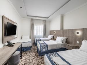 Alayam Elite Hotel في مكة المكرمة: غرفة فندقية بثلاث اسرة وتلفزيون بشاشة مسطحة