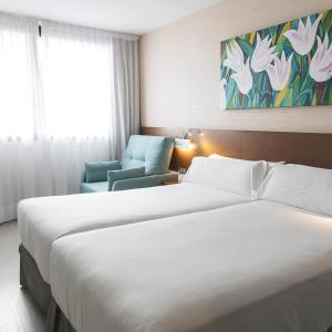 a hotel room with two beds and a chair at Hotel & Spa Real Ciudad De Zaragoza in Zaragoza