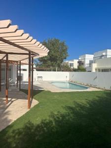 un patio trasero con piscina y pérgola de madera en LUXURY 4 Bedroom Private Pool Villa at THE WAVE en Mascate