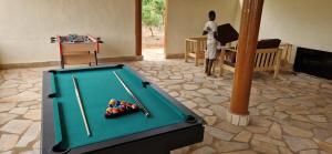 a man standing next to a pool table with cuesticks at Le Jardin de L'Atacora in Natitingou