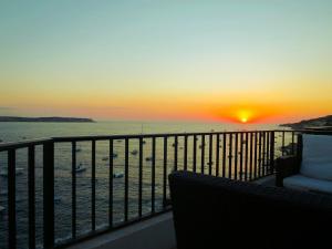a sunset over the ocean with a chair on a balcony at Seafront apartment Terrace, lounger & Panoramic ocean views in Mellieħa