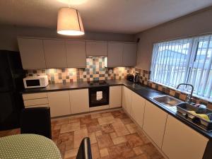 cocina con armarios blancos, fregadero y microondas en Laurelbrook Town House, en Magherafelt