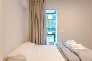 Schlafzimmer mit einem Bett mit weißer Bettwäsche und einem Fenster in der Unterkunft Vista Mar na Rua 303 em Itapema, Garagem e Wifi HU1718 in Itapema