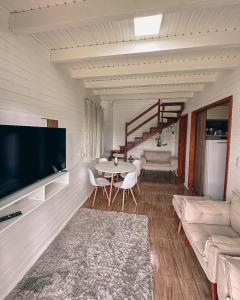 ein Wohnzimmer mit einem TV und einem Tisch mit Stühlen in der Unterkunft Chalés Florescer nos Canyons in Praia Grande