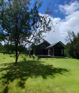 una casa en un campo con un árbol en primer plano en Casa Rural con opción de tina temperada, en Puerto Varas