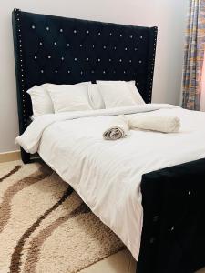 a bed with a black headboard and white sheets and pillows at Adjana’s Cozy apartment in Nairobi