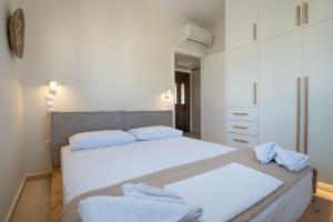 a white bedroom with two beds with towels on them at Stoupa Harmony Suites - Two Bedroom Apartment in Stoupa