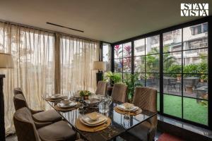 a dining room with a table and chairs and large windows at StayVista's Vogue Vista - Contemporary Chic Interiors, Terrace & Indoor-Outdoor Games in Kolkata
