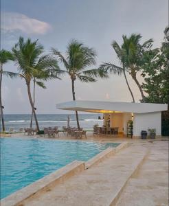 einen Pool neben einem Strand mit Palmen in der Unterkunft Juan Dolió Service Vip in Santo Domingo