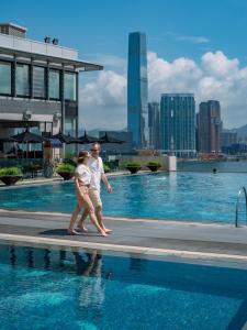 a man and a woman walking by a swimming pool at Four Seasons Hotel Hong Kong in Hong Kong