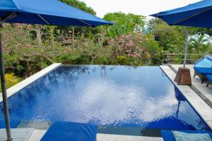 a swimming pool with a blue umbrella and chairs at Villa Penyon in Nusa Lembongan