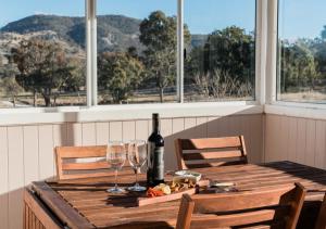 a wooden table with a bottle of wine and two glasses at Pretty Pink Queenslander - Spectacular Views, Space and Serenity in Tenterfield +38 photos