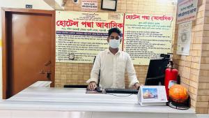 Un homme dans un masque assis à une table avec un ordinateur dans l'établissement Hotel Padma Residential Jatrabari, à Dhaka