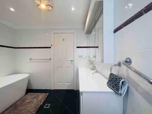 a white bathroom with a tub and a sink at Maroubra Gem Close to Everything Sleep 16 in Sydney