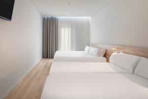 2 letti in una camera con pareti bianche e pavimenti in legno di B&B HOTEL Olhão Algarve a Olhão
