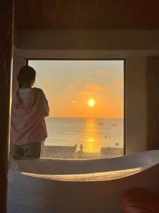 Eine Frau, die aus dem Fenster blickt, auf den Sonnenuntergang. in der Unterkunft Oceanside Villa Phuquy Island in Cu Lao Thu