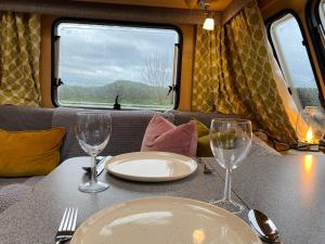 a table with plates and wine glasses on a train at Cosy Caravan on Luxury Campsite in Hulme End