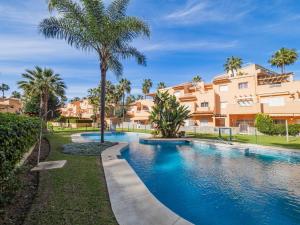 a swimming pool with palm trees in front of a building at Cubo's Cabopino Beach Marbella Apartment in Marbella