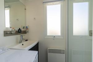 a white bathroom with a sink and a mirror at Mobil-home in Les Mathes