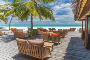 Meeru Maldives Resort Island في ديفوشي: سطح خشبي مع كراسي وطاولات على الشاطئ