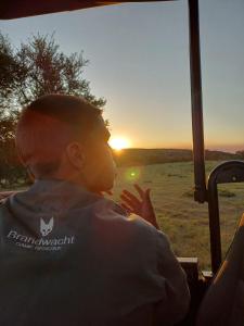 un homme assis dans un véhicule en regardant le coucher du soleil dans l'établissement Garden Route Safari Camp, à Mossel Bay
