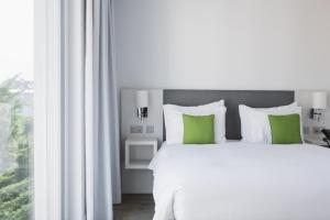 a white bed with green pillows next to a window at Base Vevey in Vevey