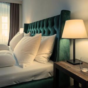 a bed with a green headboard and a table with a lamp at Hotel Forstinger - Boutique Hotel Schärding in Schärding