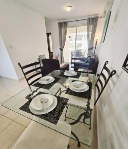 una mesa de comedor y sillas con una mesa de cristal y platos. en Delightful Poolside apartment, en Pafos