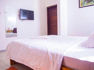 a bedroom with a white bed with a tv on the wall at Explorers Hub in Kampala