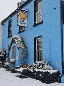 un edificio azul cubierto de nieve con un banco delante en The Ship Inn, en Bardsea