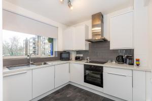 a white kitchen with white cabinets and a sink at Newly refurbished 2BR wbalcony in Vibrant Peckham in London