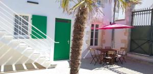 a table and umbrella next to a building with a palm tree at Les logis de Simon in La Flotte